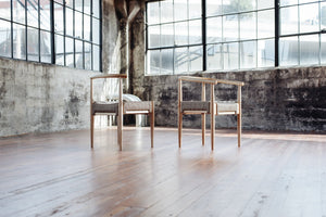 two Harbor Chairs made of white oak and grey woven rope seats sit in an empty warehouse near windows